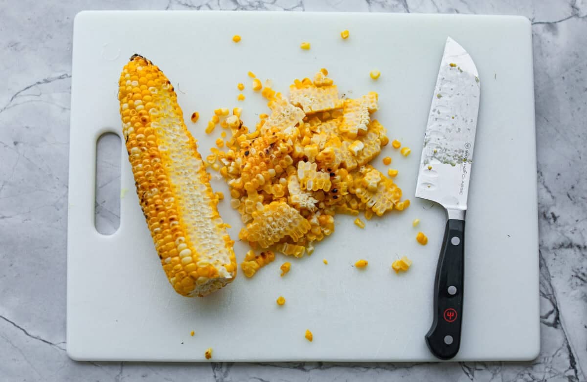 I love salads in the summer, and this grilled shrimp salad is such a good one. It’s fresh, colorful, and filling without feeling heavy. And the dressing? Oh my gosh. The chipotle-lime flavor is so good, you’ll want to pour it on everything. Cutting board with a cob of corn with a pile of kernels cut off with a large knife.
