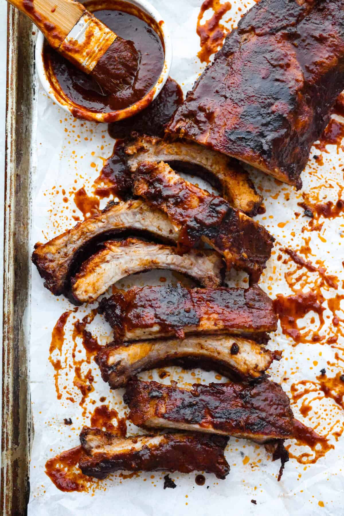 These grilled BBQ ribs are what summer cookouts are all about! Slow-cooked until fall-off-the-bone tender, then finished with a sticky, caramelized layer of BBQ sauce that'll have everyone licking their fingers. Slab of grilled BBQ ribs with a small bowl of sauce and a basting brush.