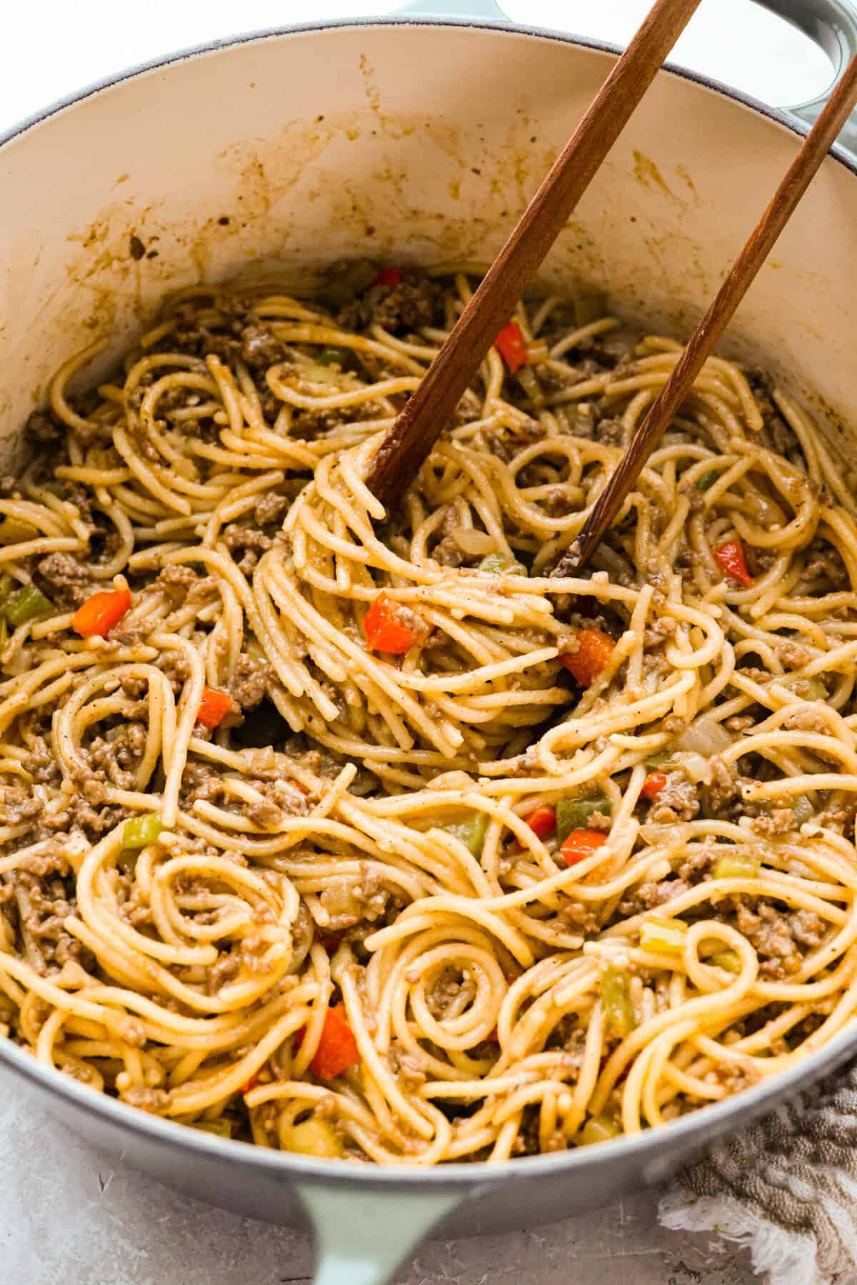 Pot of dirty spaghetti being stired with wooden tongs. 