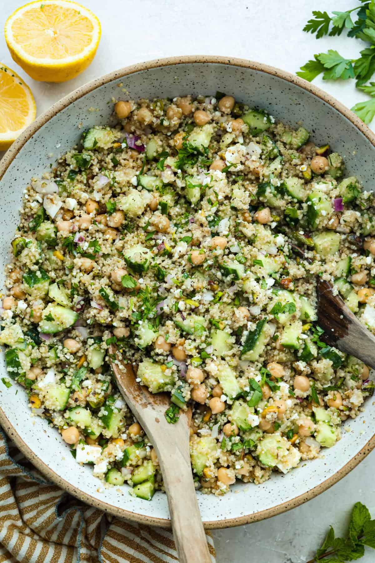This Jennifer Aniston Salad is light, fresh, and perfect for summer lunches. It’s packed with veggies, chickpeas, herbs, pistachios, and feta, then tossed in a simple lemon dressing that makes everything taste bright and delicious. Large bowl of Jennifer Aniston salad with wooden serving spoon.