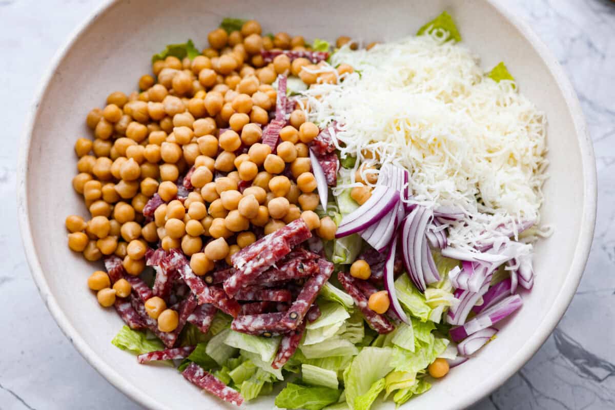 This copycat La Scala Salad is the famous Italian chopped salad from Beverly Hills that Kim Kardashian is rumored to love. Itโs fresh, crunchy, and packed with chickpeas, salami, mozzarella, and zesty red wine vinaigrette. Salad ingredients added to a large bowl.