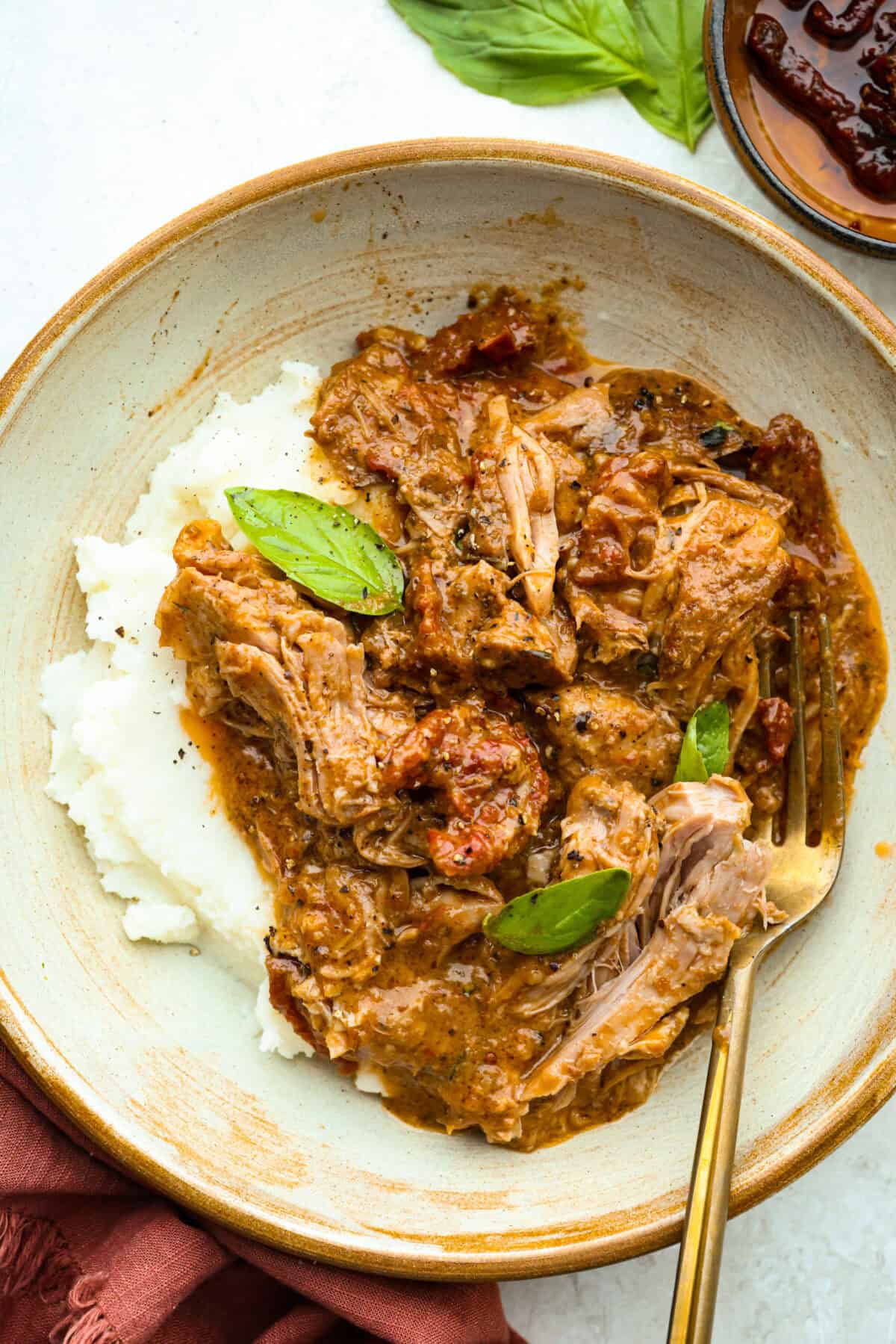 Marry Me Pork Roast lives up to its name! Tender pork, slow cooked in a creamy, garlicky sun-dried tomato sauce that's so good! Pile it over mashed potatoes or buttered noodles to soak up every drop. Plate with Marry Me Pork roast serving over mashed potatoes and a gold fork.