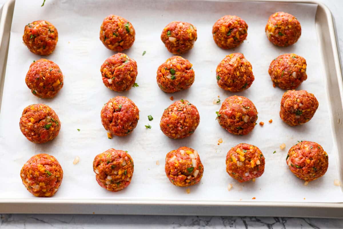 Scooped and shaped meatballs on a parchment lined baking sheet. 