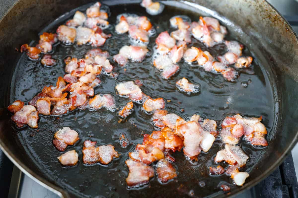 Bacon pieces cooking in a skillet.