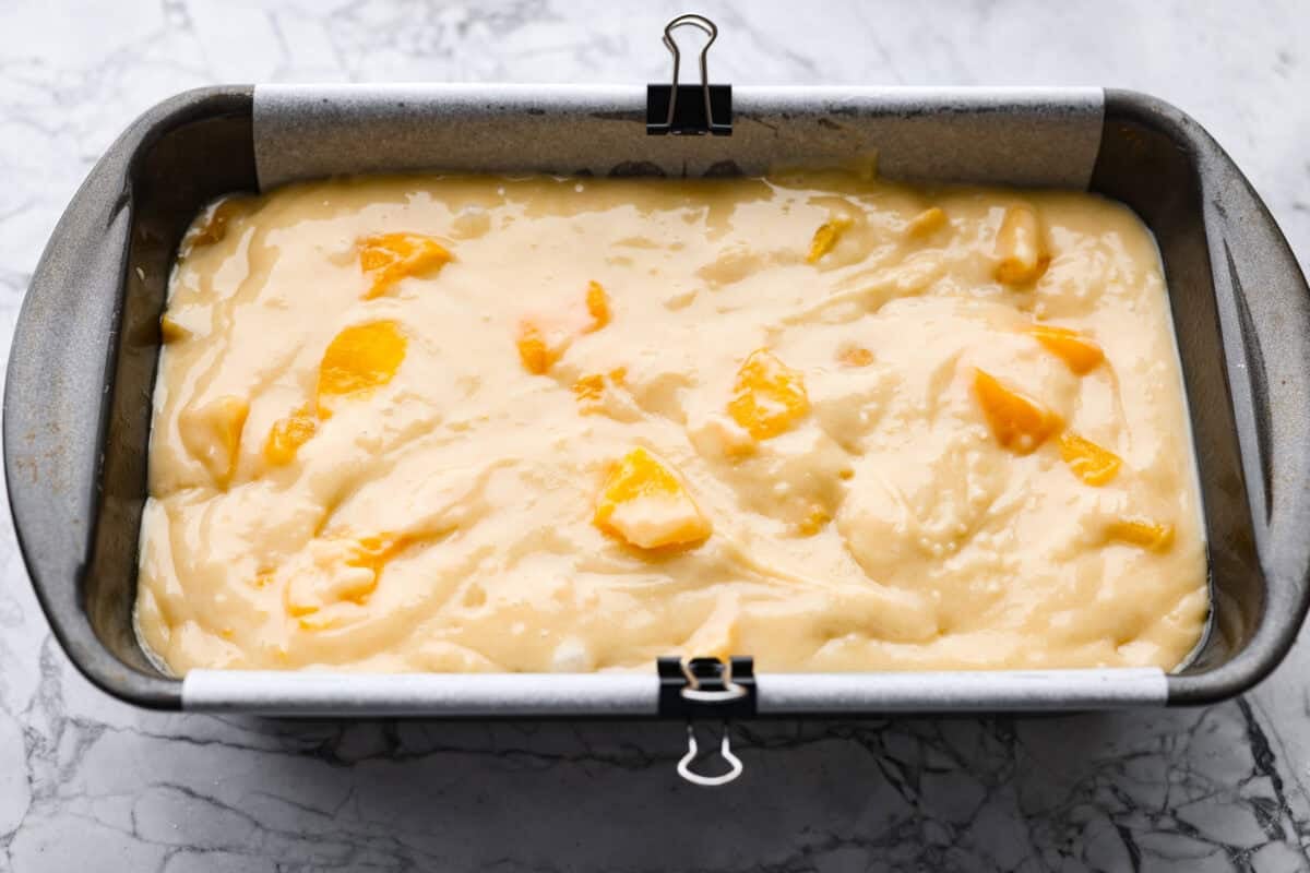 If you love peaches, this peach loaf belongs on your baking list! It’s incredibly moist, packed with sweet peaches, and topped with a peach glaze that makes every slice even more irresistible. Peach loaf batter in a baking pan.
