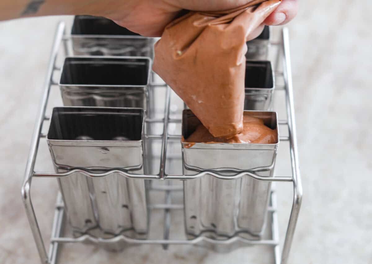 Pudding pops instantly take me back to summer as a kid! They’re cold, creamy, chocolatey, and easy to make with just a few simple ingredients. Keep a batch in the freezer for hot afternoons or an easy after-dinner treat. Someone squeezing the pudding mixture into the popsicle molds.