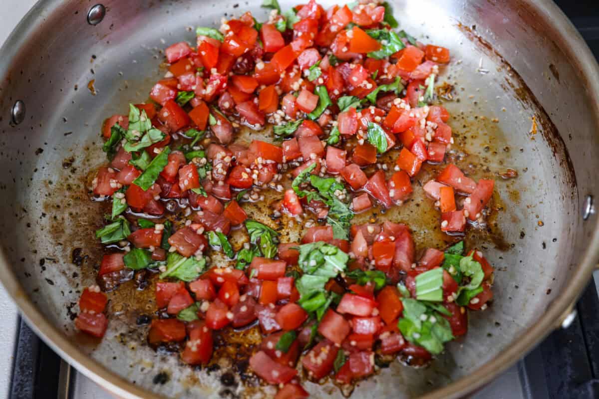 If you have fresh summer tomatoes sitting on your counter, this is your sign to make this Bruschetta Chicken Pasta. It's light, fresh, and shows that simple ingredients can make the best meals. Tomato and basil and garlic cooking in a skillet.
