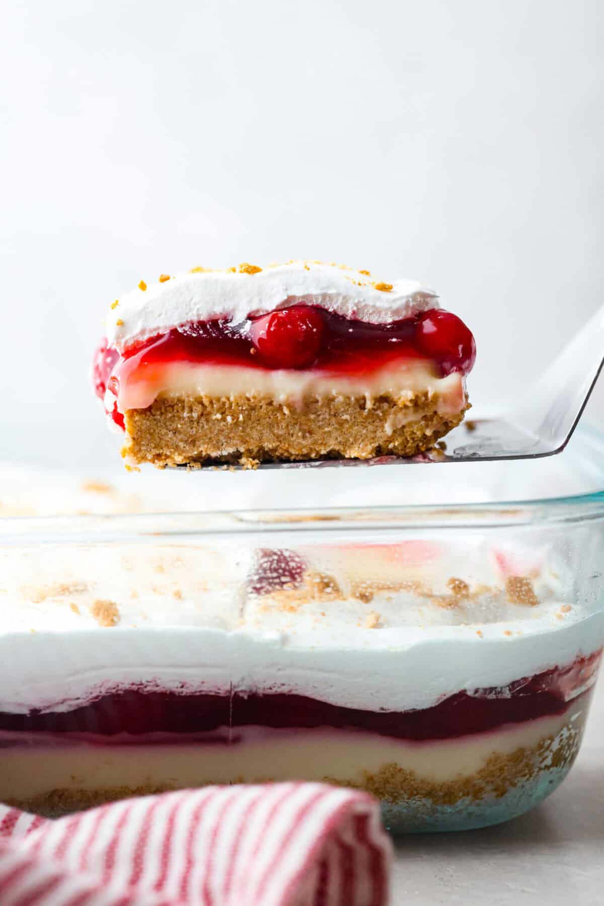 Someone lifting a slice of cherry cheesecake lush out of the glass dish.