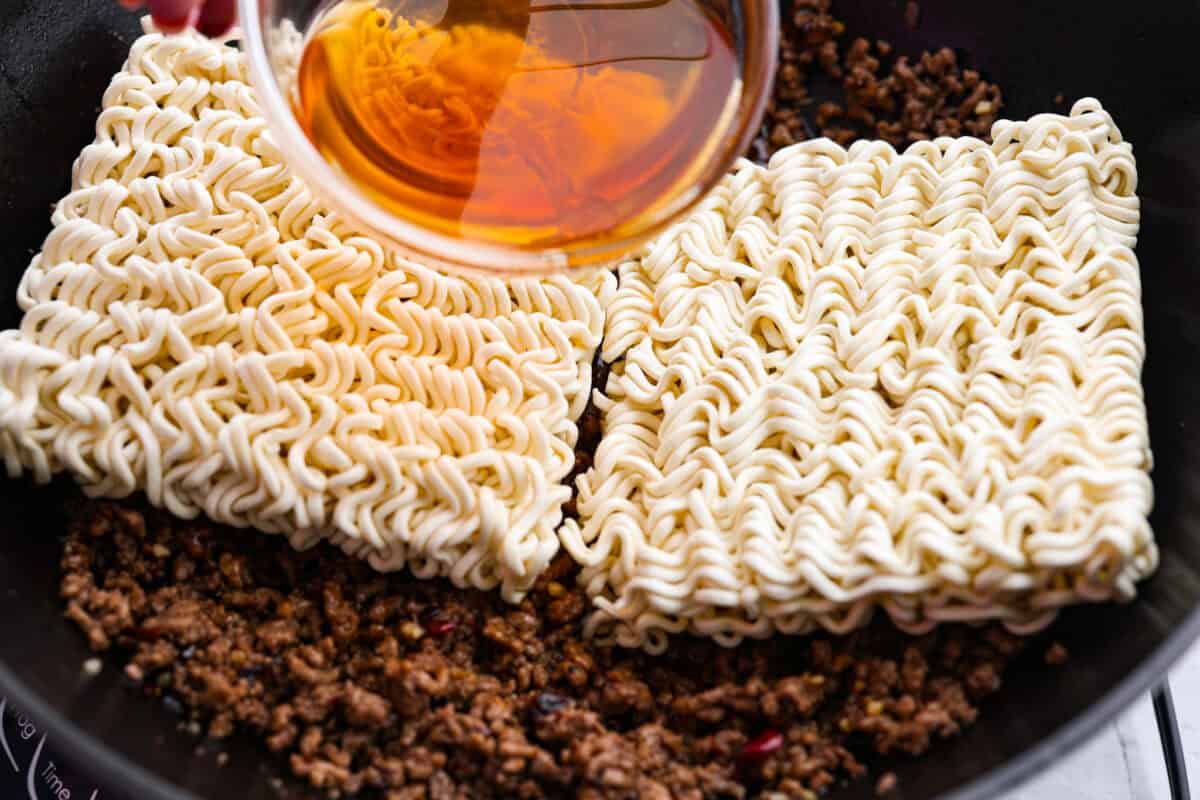 Ramen noodles placed on top of the ground beef and then beef broth being added to steam the noodles. 