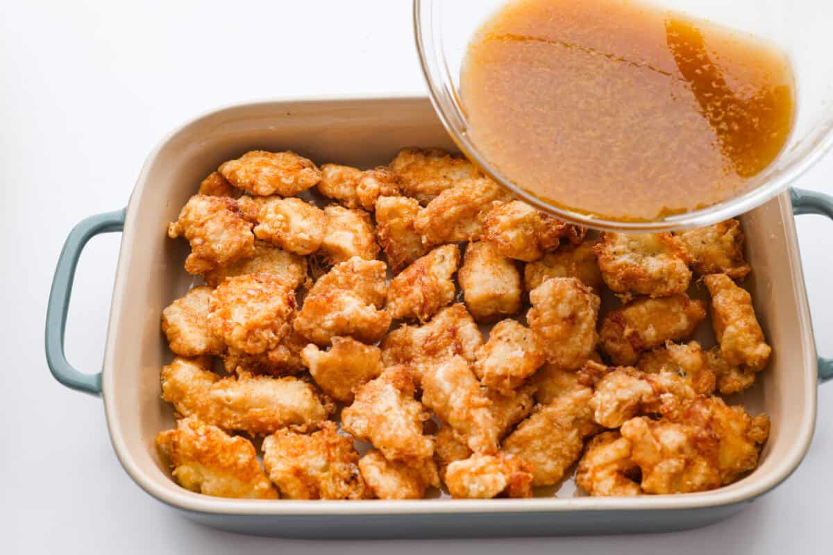 Someone pouring the lemon sauce over the browned fried chicken pieces in a 9x13 pan. 