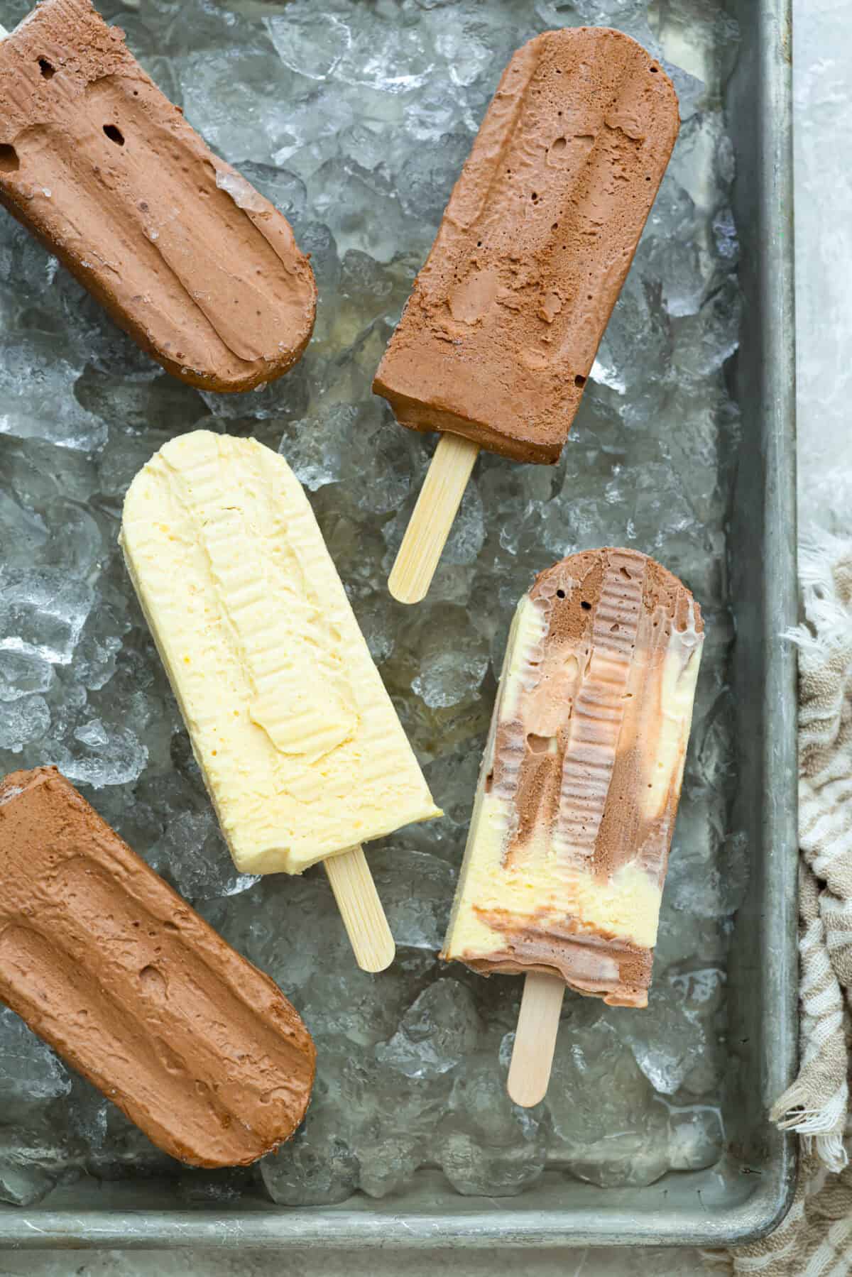 Pudding pops instantly take me back to summer as a kid! They’re cold, creamy, chocolatey, and easy to make with just a few simple ingredients. Keep a batch in the freezer for hot afternoons or an easy after-dinner treat. Top down image of pudding pops on a cookie sheet covered in ice t o keep them cold.