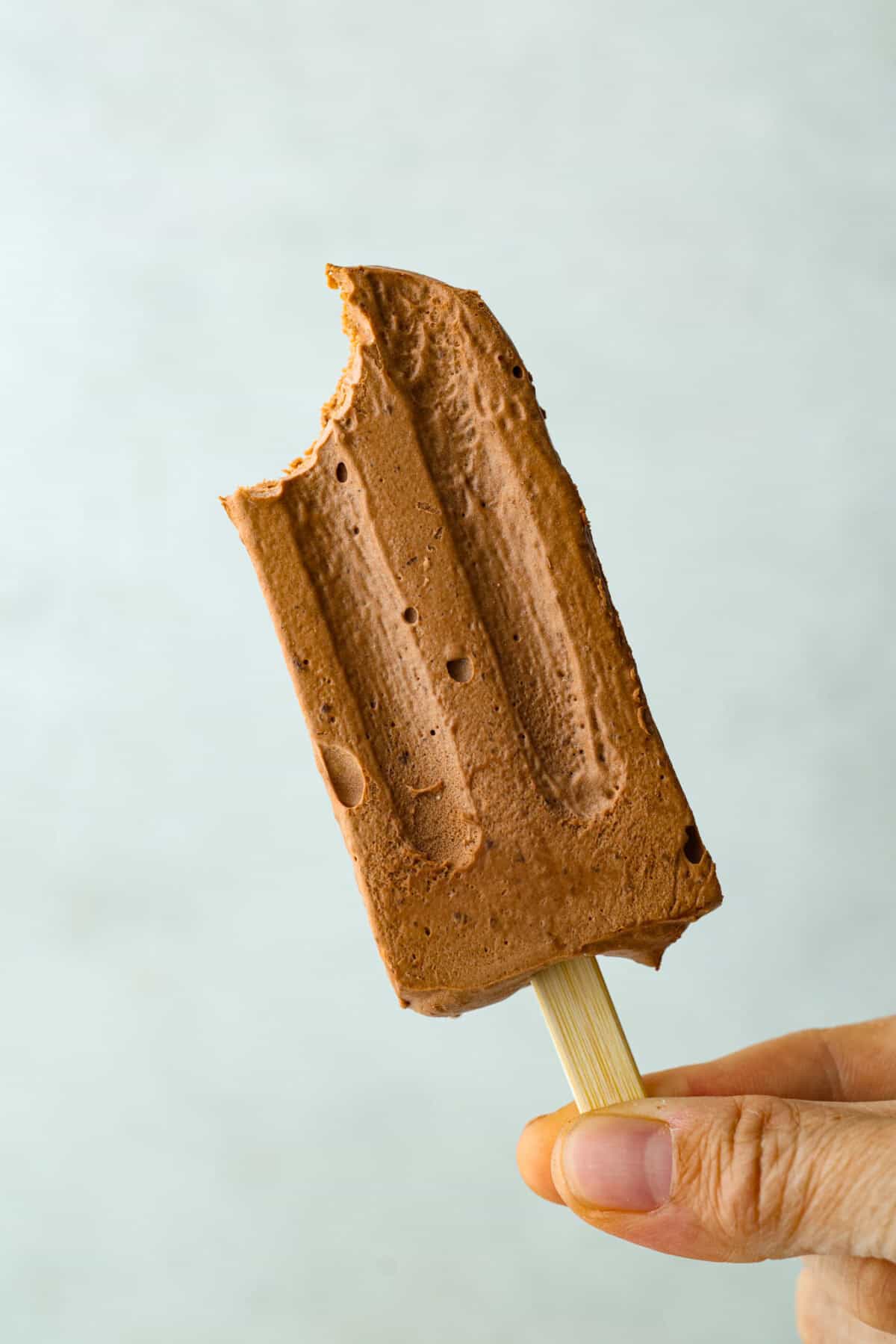Pudding pops instantly take me back to summer as a kid! They’re cold, creamy, chocolatey, and easy to make with just a few simple ingredients. Keep a batch in the freezer for hot afternoons or an easy after-dinner treat. Someone holding up a pudding pop with a bite taken out of it.