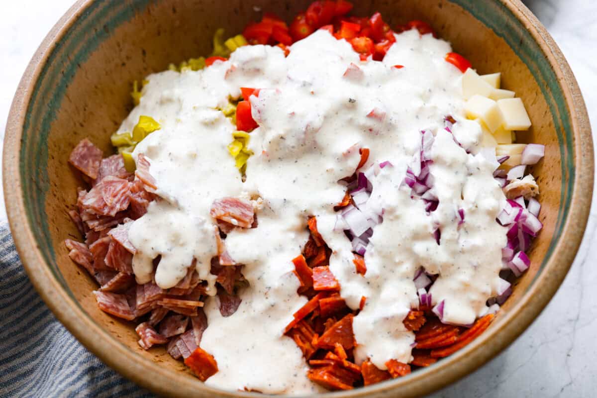 I know you guys love my famous grinder sliders. This grinder chicken salad brings all those bold flavors into one easy recipe. It's hearty, creamy, and perfect for lettuce wraps or a quick lunch straight from the bowl. Dressing added to the top of the salad ingredients.