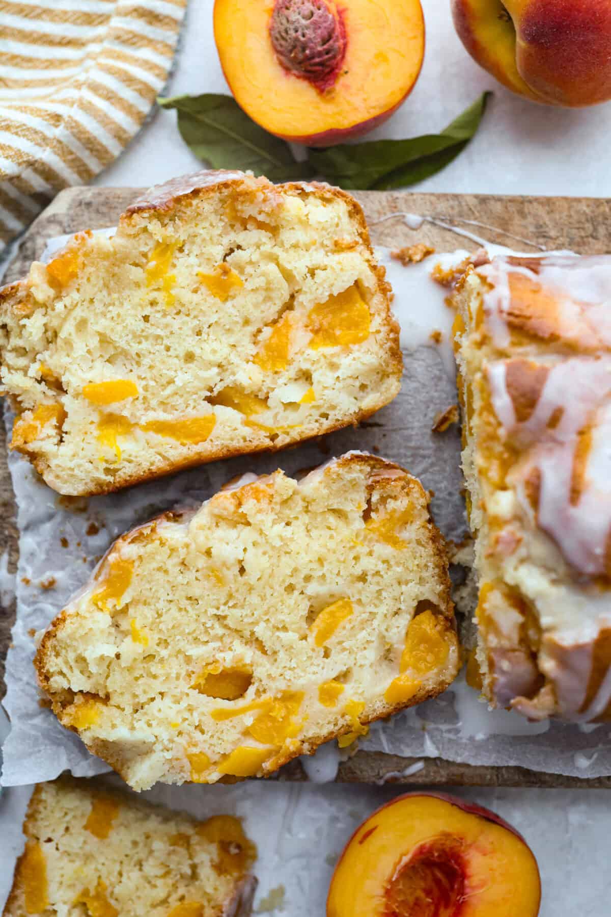 If you love peaches, this peach loaf belongs on your baking list! It’s incredibly moist, packed with sweet peaches, and topped with a peach glaze that makes every slice even more irresistible. Overhead shot of two slices of peach loaf on a cutting board surrounded by fresh peaches.