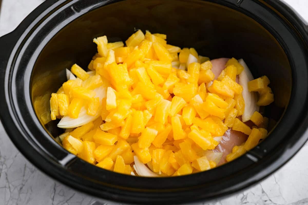 Slow cooker Aloha chicken is sweet, smoky, and so easy to throw together! Tender chicken cooks with pineapple, onion, and barbecue sauce until itβs full of flavor and ready to shred. Serve it over rice for a simple dinner the whole family will love. Pineapple and onion added to the crockpot.