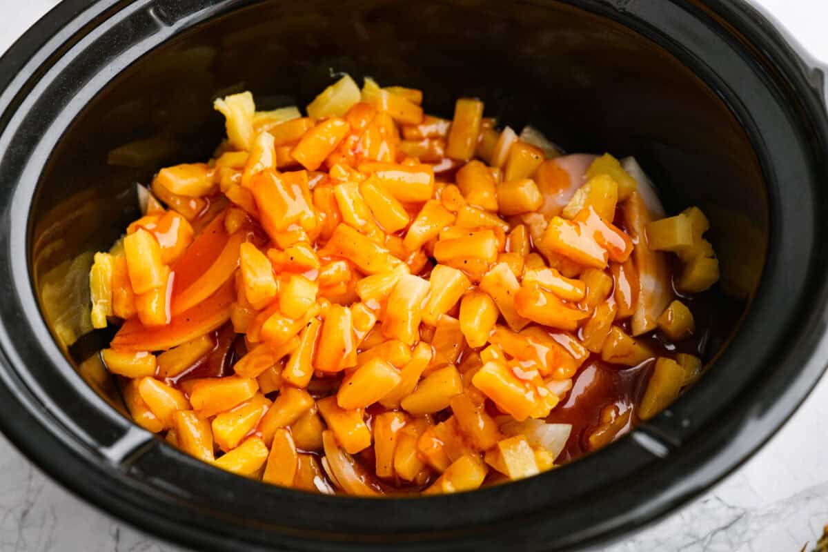 Slow cooker Aloha chicken is sweet, smoky, and so easy to throw together! Tender chicken cooks with pineapple, onion, and barbecue sauce until itβs full of flavor and ready to shred. Serve it over rice for a simple dinner the whole family will love. Sauce poured over the pineapple, onion, and chicken in the slow cooker.