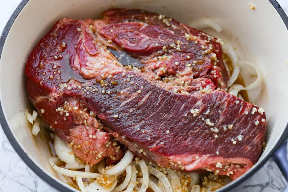 Caramelized chuck roast is everything I want in a cozy dinner. The beef cooks low and slow until it practically falls apart, then gets sprinkled with brown sugar and broiled until the edges are sticky, caramelized, and SO good. Chuck roast, onions, garlic and sauce added to the dutch oven.