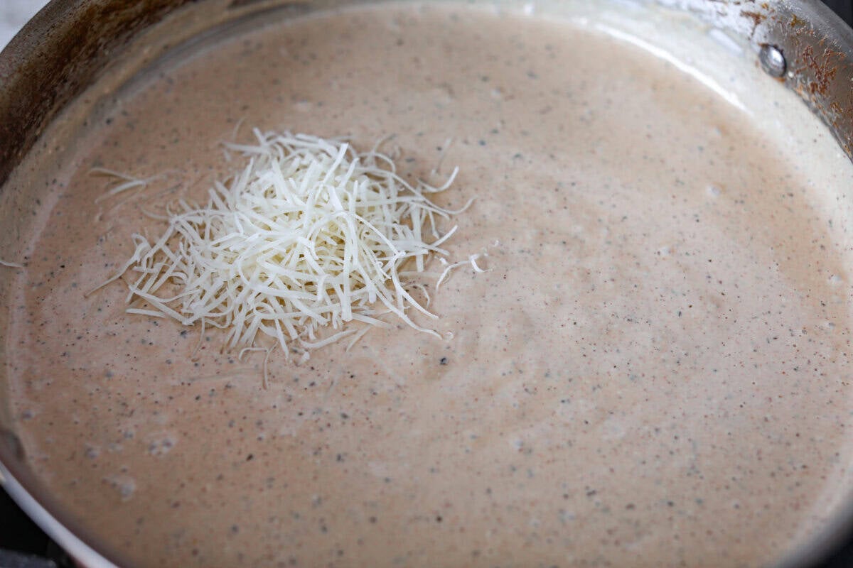 Adding cheese to the sauce in the skillet.