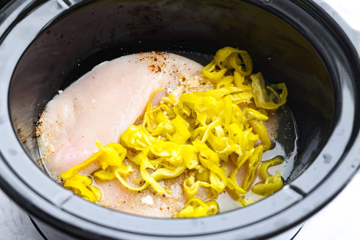 Crockpot Italian grinder chicken is an easy dinner packed with bold, tangy Italian flavor. Tender shredded chicken turns creamy and delicious in the slow cooker. Serve it on toasted hoagie rolls or over pasta for a simple family dinner. Slow cooker full of the ingredients.