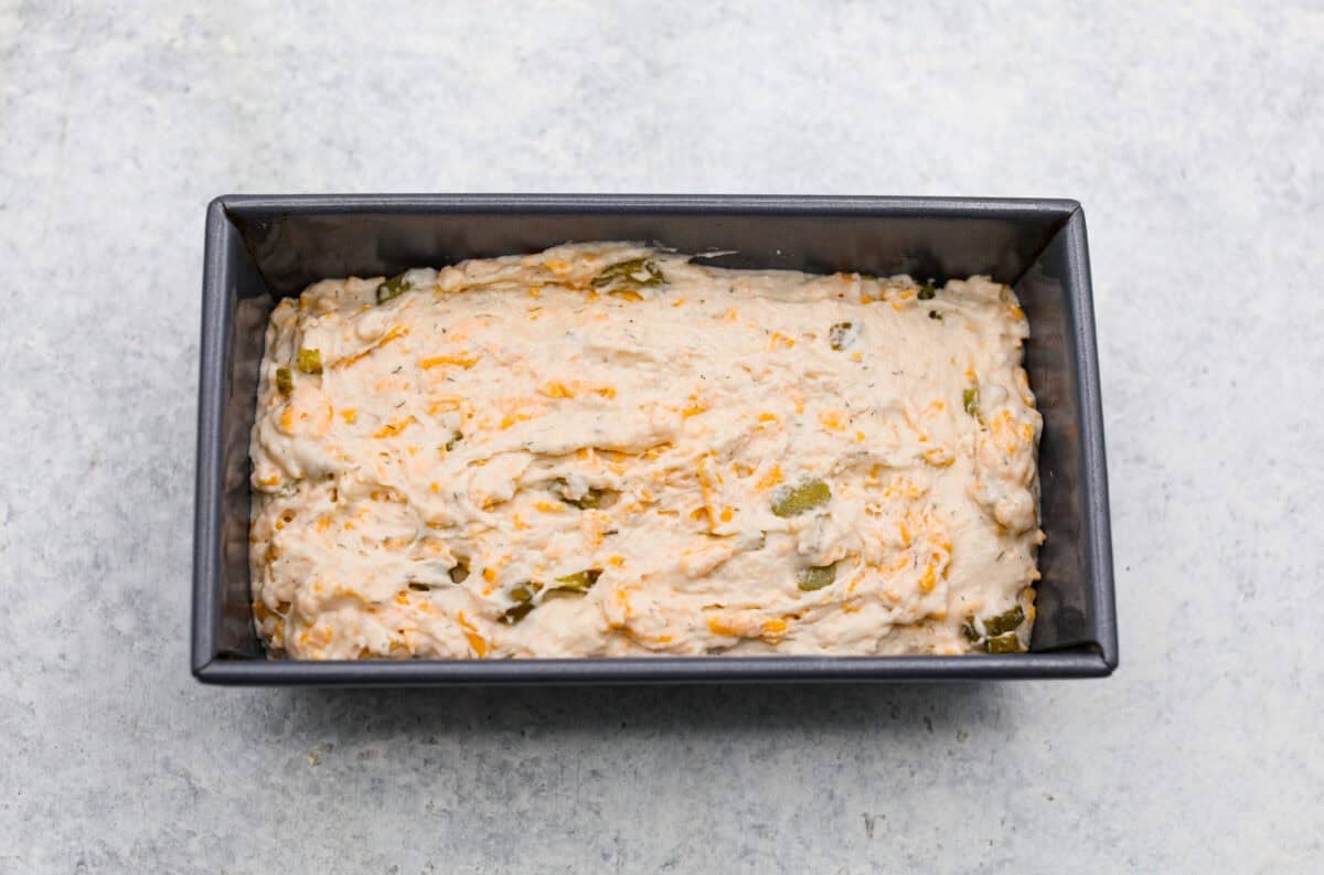 Dill pickle bread is cheesy, buttery, and packed with tangy pickle flavor in every bite. Chopped dill pickles and my secret dill pickle seasoning give this easy quick bread even more bold, briny flavor, with plenty of melty cheese. Dill pickle bread dough added to a loaf pan.