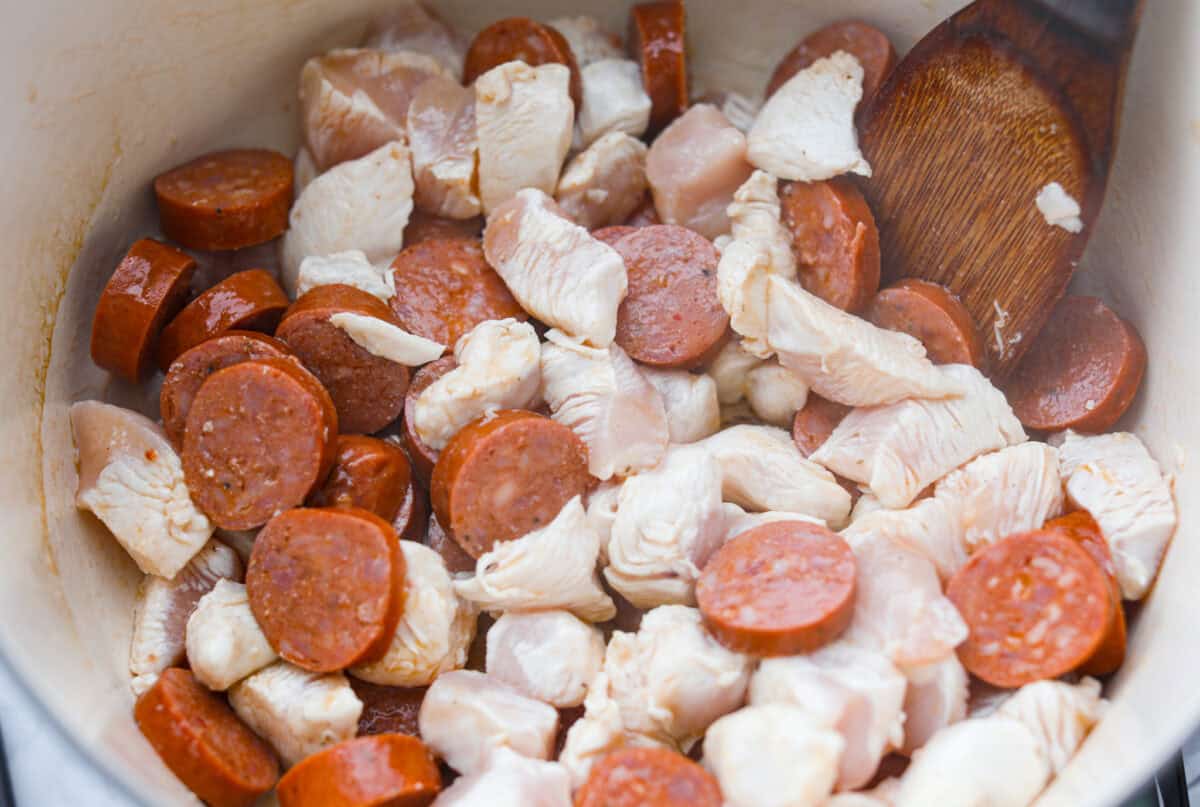 Dutch oven with sausage and chicken cooking in it. 