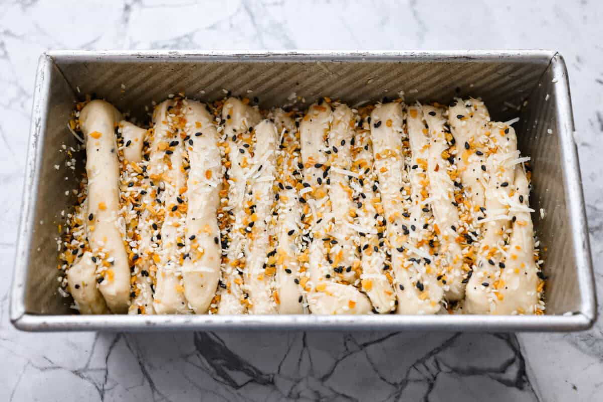 Everything bagel pull apart bread is soft, cheesy, and loaded with savory flavor in every layer. The homemade dough is stacked with Parmesan cheese and everything bagel seasoning, then baked until golden and fluffy. Dough stacks added to the loaf pan and topped with more everything bagel seasoning and cheese.