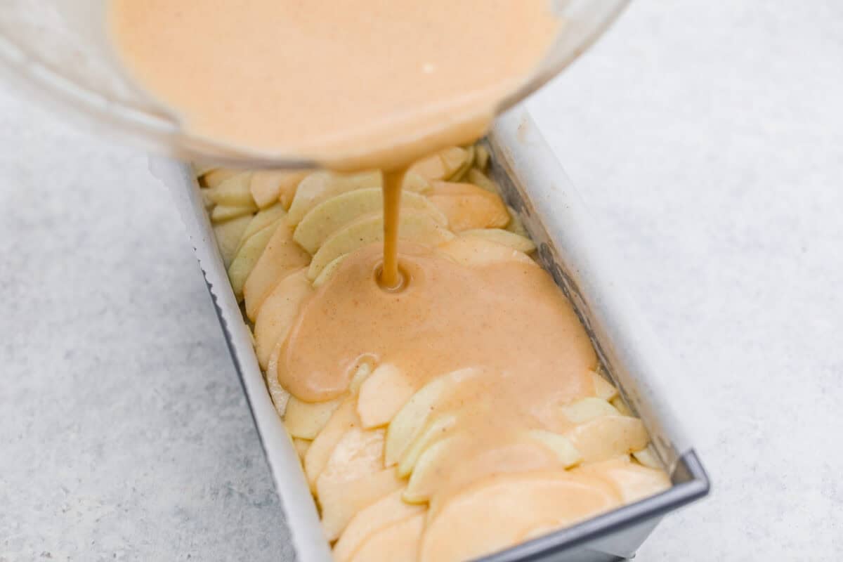 This invisible apple cake is a little magical! Paper-thin apple slices are coated in a simple, lightly spiced batter, then layered in a loaf pan and baked into a tender, custardy cake. Such a delicious way to enjoy fresh apples! Pouring extra bater into the loaf pan with the apple mixture.