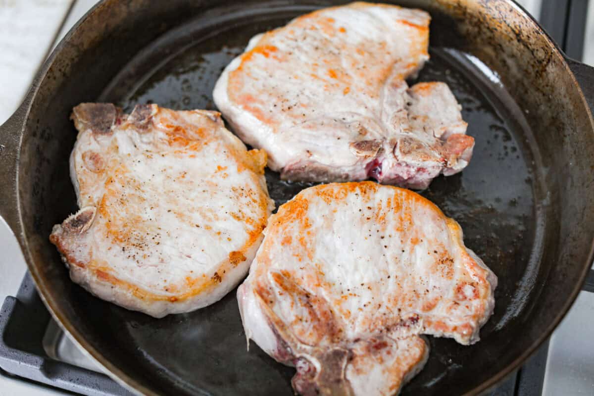 Searing pork chops in a skillet.
