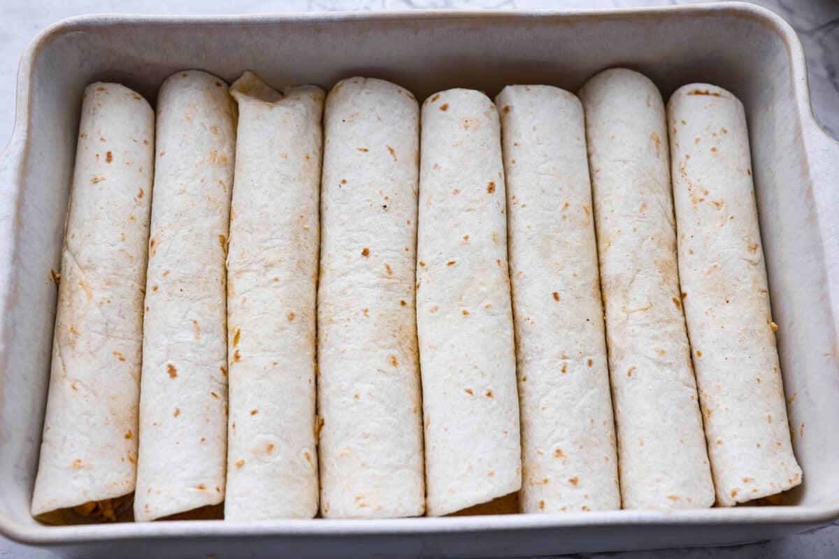 Tortillas filled with enchilada mixture added to the baking dish. 