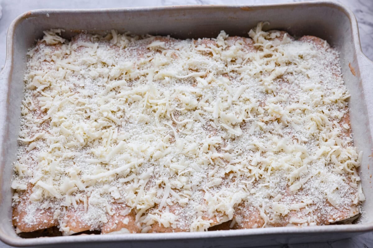 Filled tortillas covered with sauce and cheese ready to go in the oven.