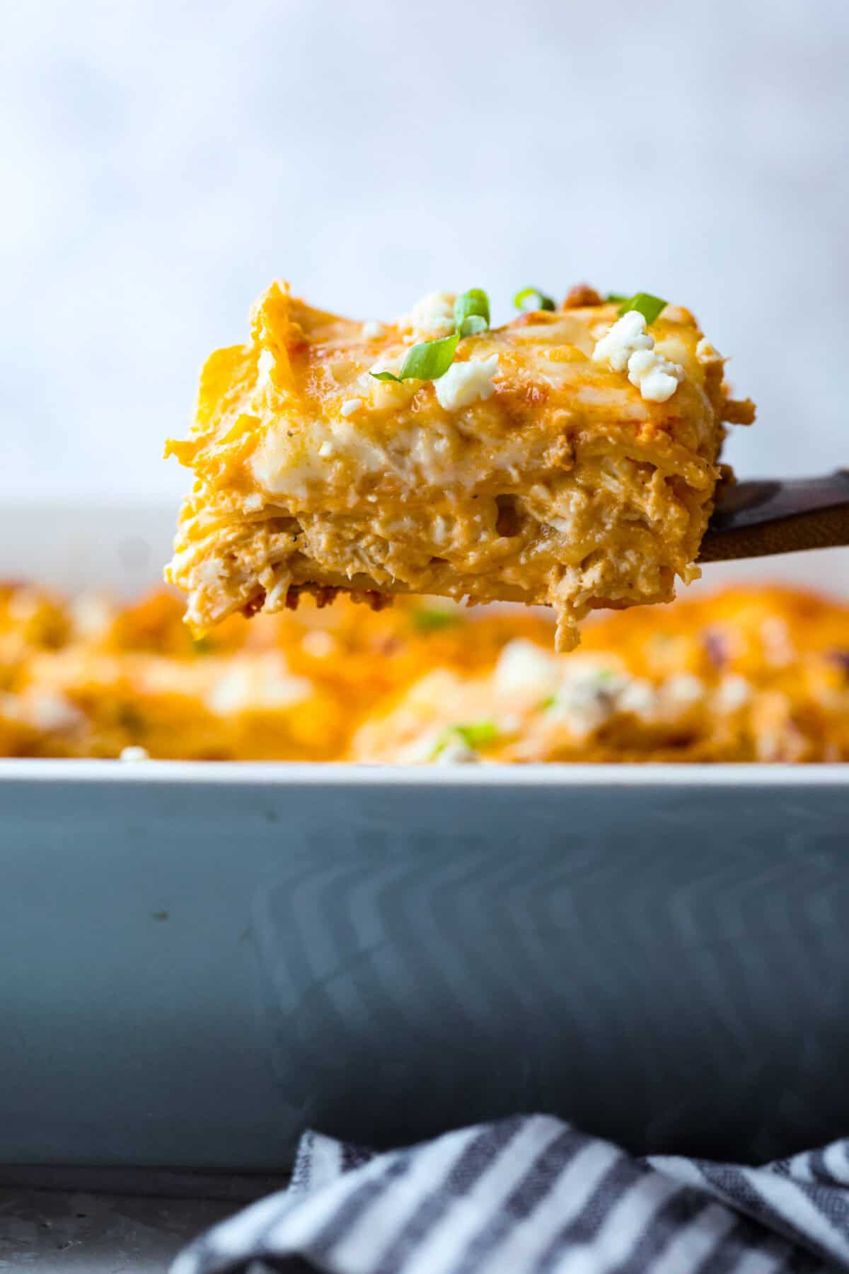 Side shot of a slice of buffalo chicken lasagna being lifted out of the baking dish. 
