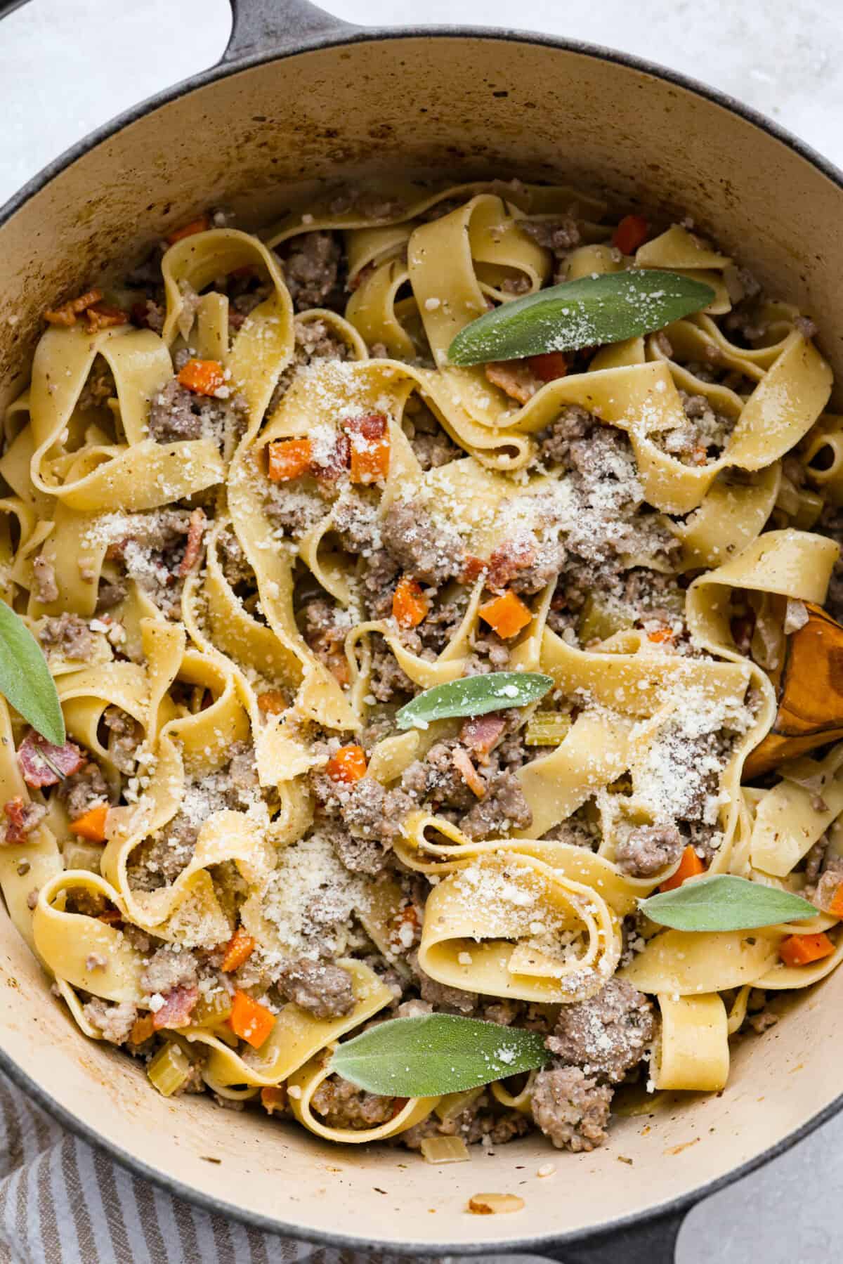 No tomatoes, no red sauce, just a rich, savory white bolognese loaded with beef, pork, bacon, white wine, and plenty of Parmesan. Tossed with noodles, it’s a fun and seriously delicious twist on classic Bolognese. Pot of white bolognese sprinkled with parmesan cheese and sage leaves.