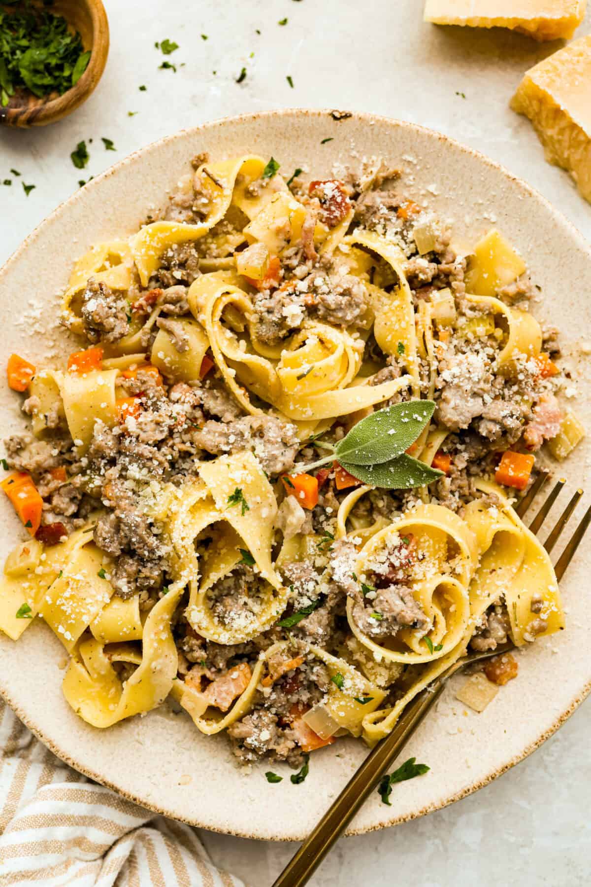 Plated white bolognese dusted with parmesan cheese and garnished with fresh sage. 