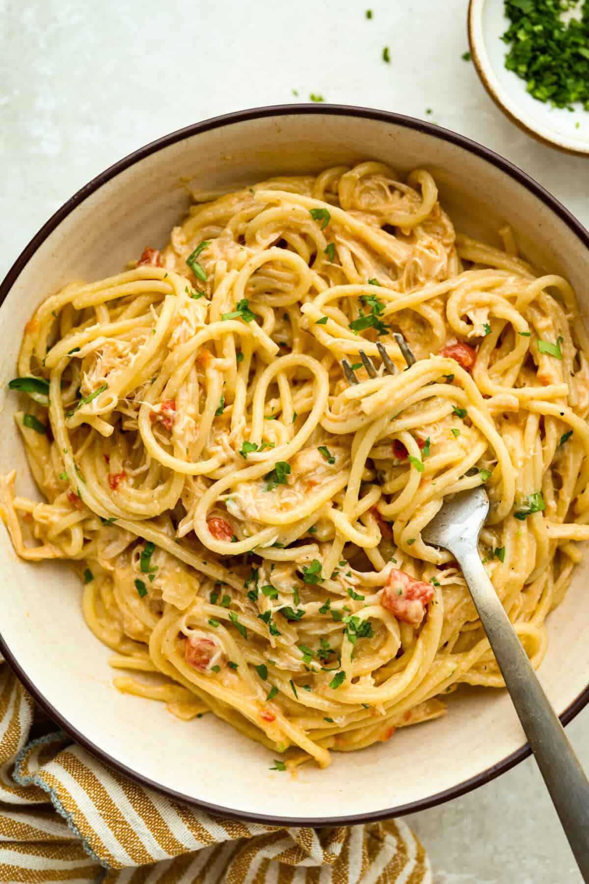 This crockpot chicken spaghetti will have everyone running to the dinner table! The slow cooker does the work while the chicken becomes tender and flavorful, then it's tossed with spaghetti, melty cheese, and a creamy sauce. Bowl with a serving of crockpot chicken spaghetti.