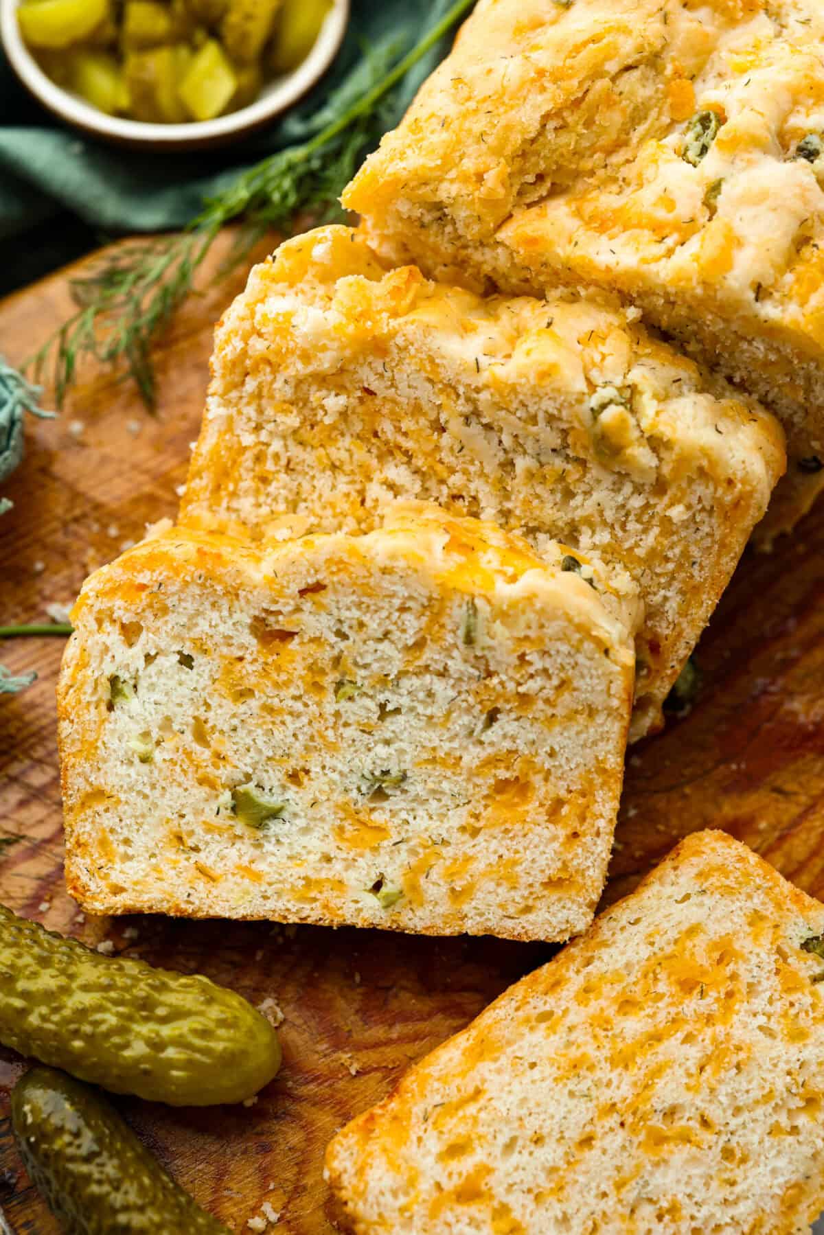 Dill pickle bread is cheesy, buttery, and packed with tangy pickle flavor in every bite. Chopped dill pickles and my secret dill pickle seasoning give this easy quick bread even more bold, briny flavor, with plenty of melty cheese. Overhead shot of dill pickle bread on a cutting board with some slices cut.