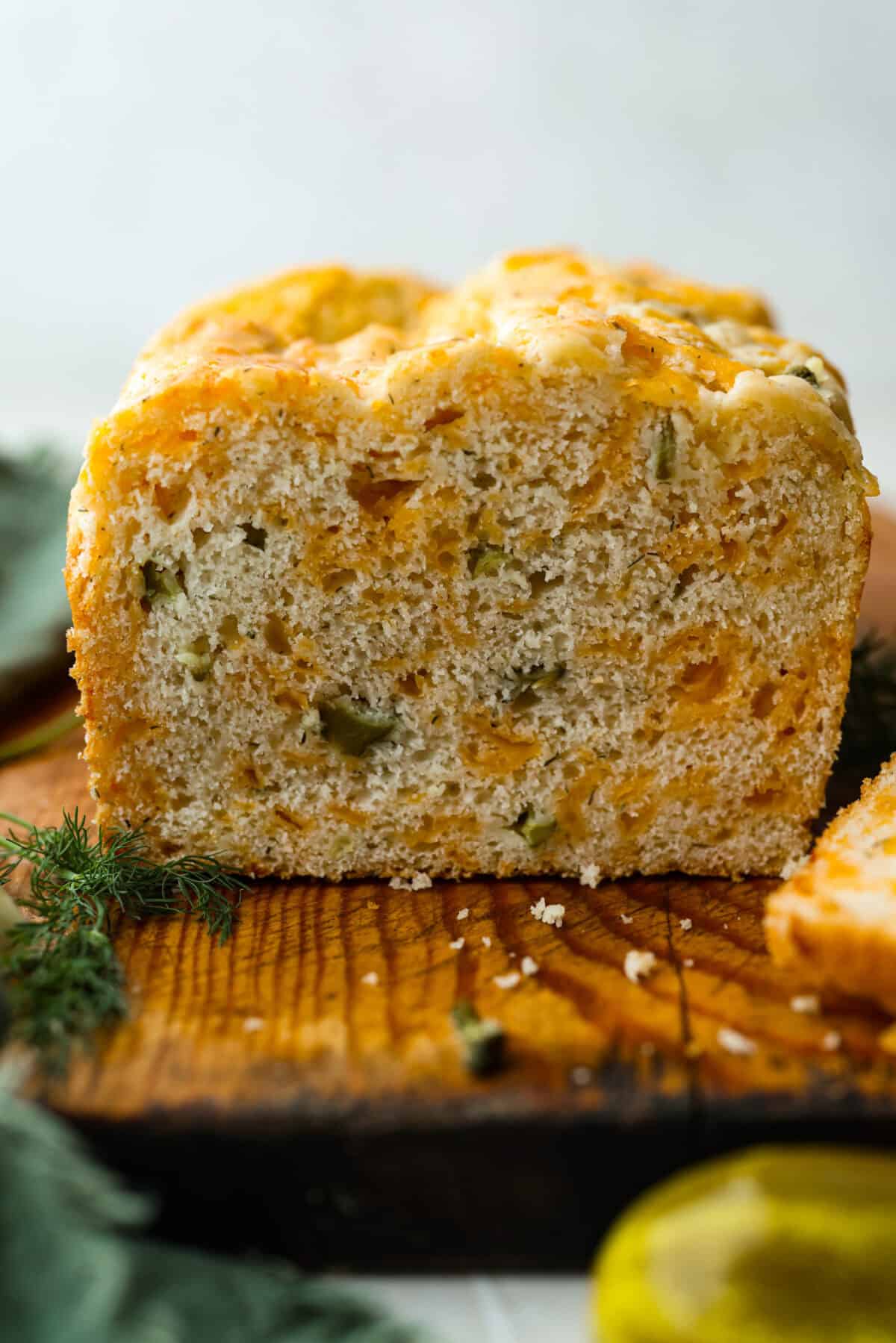 Dill pickle bread is cheesy, buttery, and packed with tangy pickle flavor in every bite. Chopped dill pickles and my secret dill pickle seasoning give this easy quick bread even more bold, briny flavor, with plenty of melty cheese. Side view of the cut loaf.