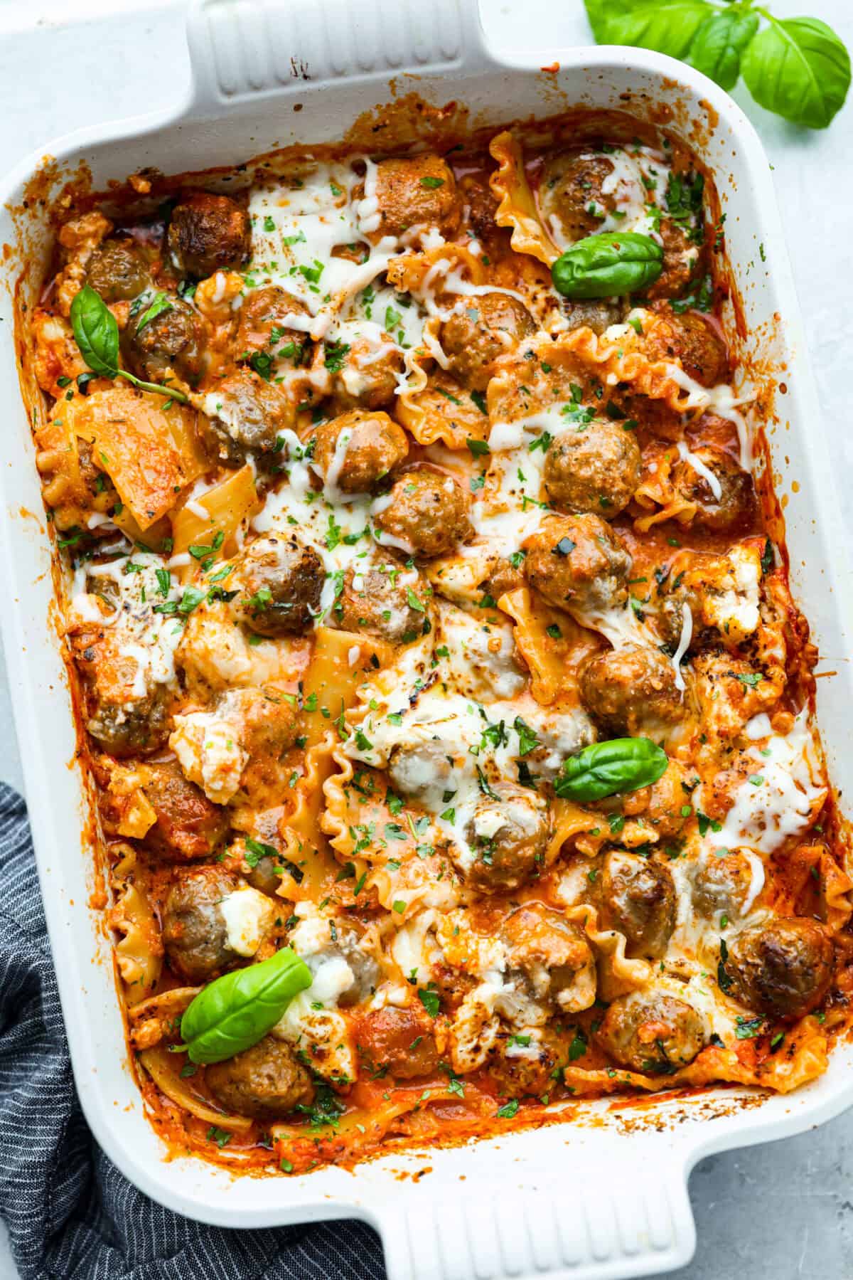 Overhead shot of lazy meatball lasagna in a baking dish garnished with basil. 