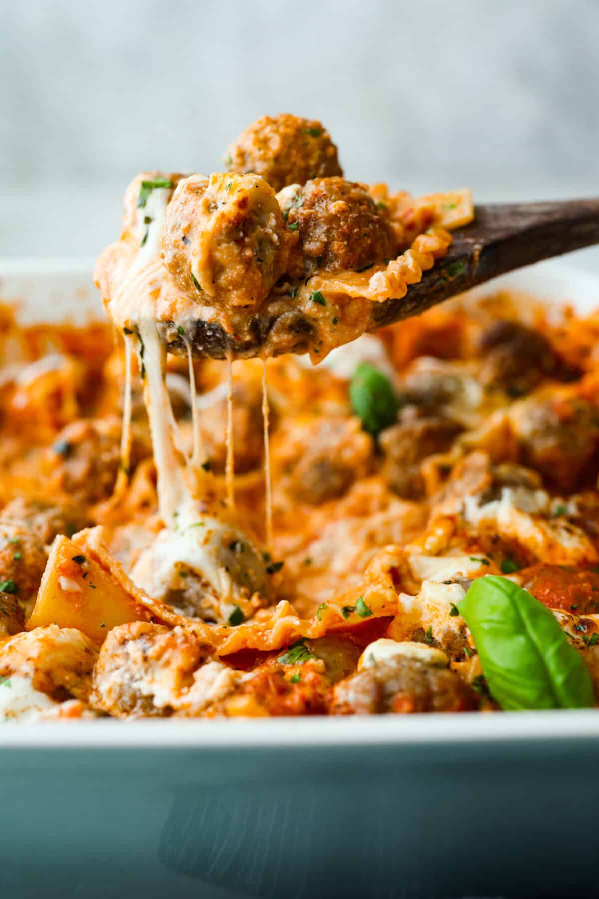 Someone lifting up a large spoonful of lazy meatball lasagna with cheese stretching in between.