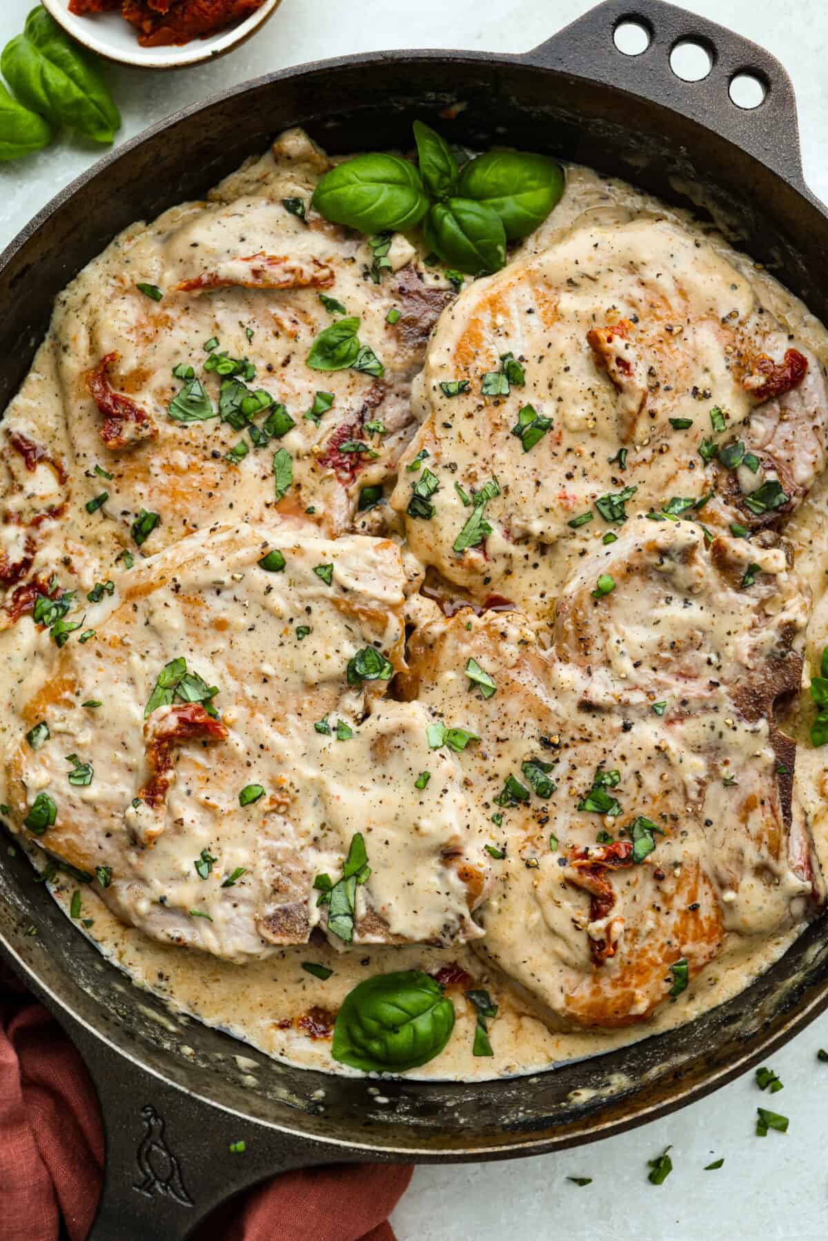 Skillet with Marry Me pork chops all cooked and ready to eat, garnished with fresh basil. 
