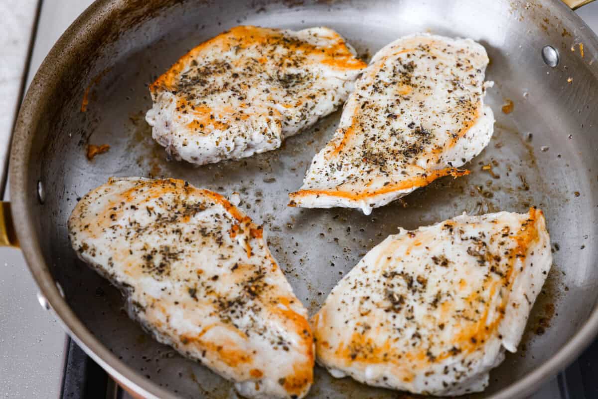 Creamy pepperoncini chicken is an easy one-skillet dinner packed with flavor! Tender chicken is smothered in a rich Parmesan cream sauce with bell peppers and tangy pepperoncini. It's the perfect balance of creamy, savory, and zesty flavor. Chicken breast cooking in a skillet.