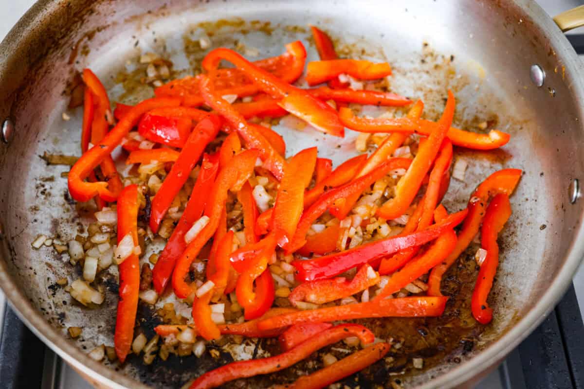 Creamy pepperoncini chicken is an easy one-skillet dinner packed with flavor! Tender chicken is smothered in a rich Parmesan cream sauce with bell peppers and tangy pepperoncini. It's the perfect balance of creamy, savory, and zesty flavor. Peppers and onions cooking in a skillet.