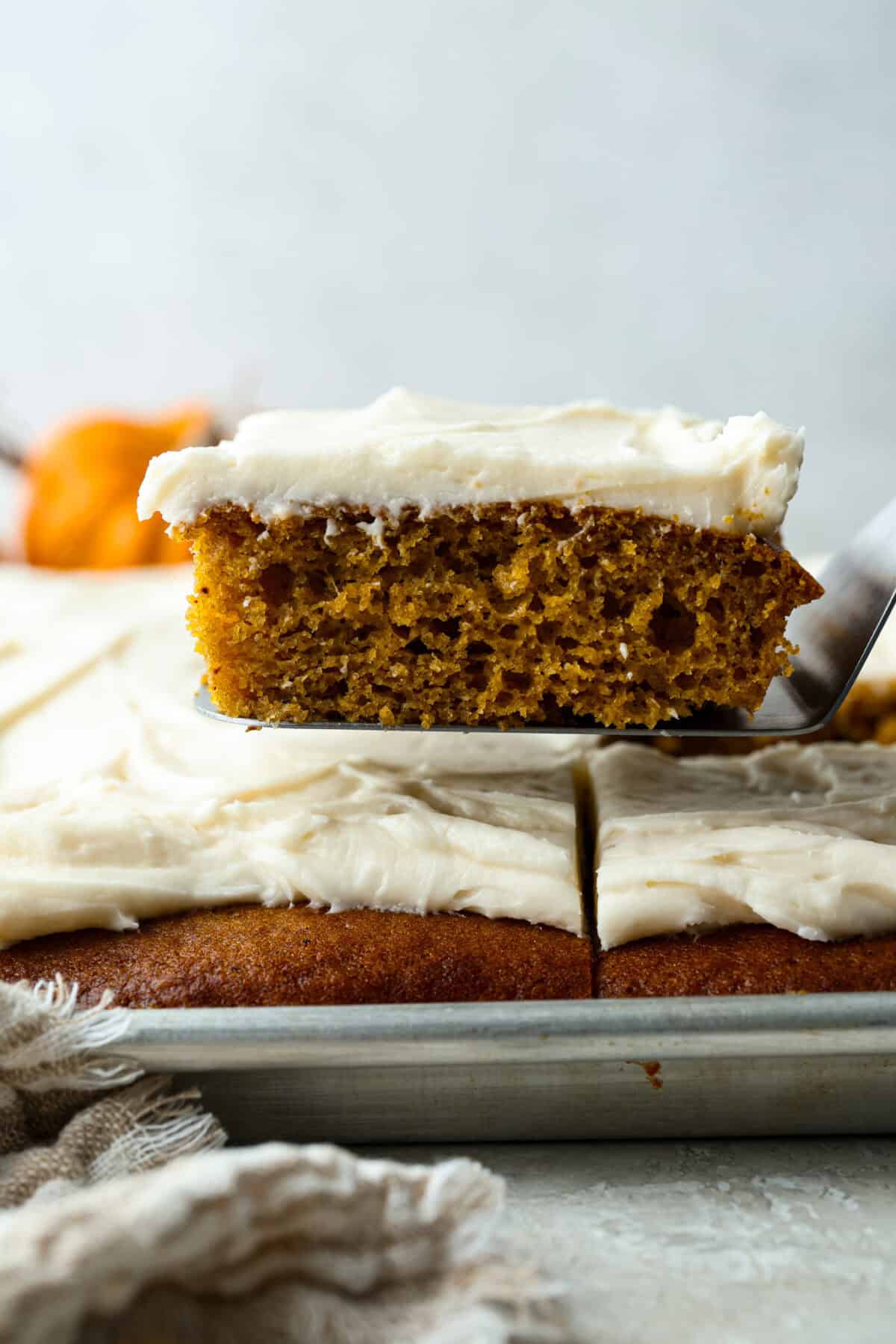 Someone lifting a slice of pumpkin sheet cake bar out of the pan. 