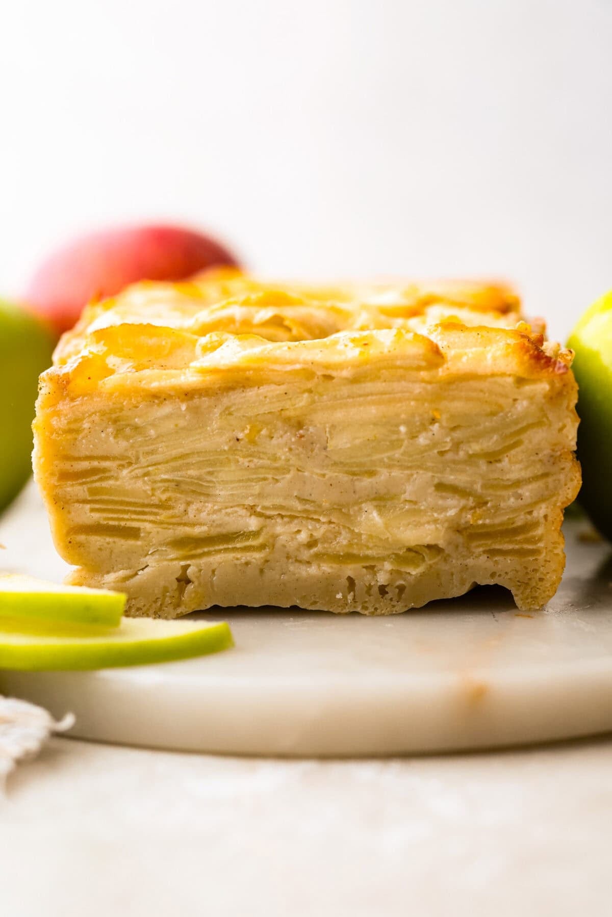 This invisible apple cake is a little magical! Paper-thin apple slices are coated in a simple, lightly spiced batter, then layered in a loaf pan and baked into a tender, custardy cake. Such a delicious way to enjoy fresh apples! Side side of a slice through invisible apple cake.