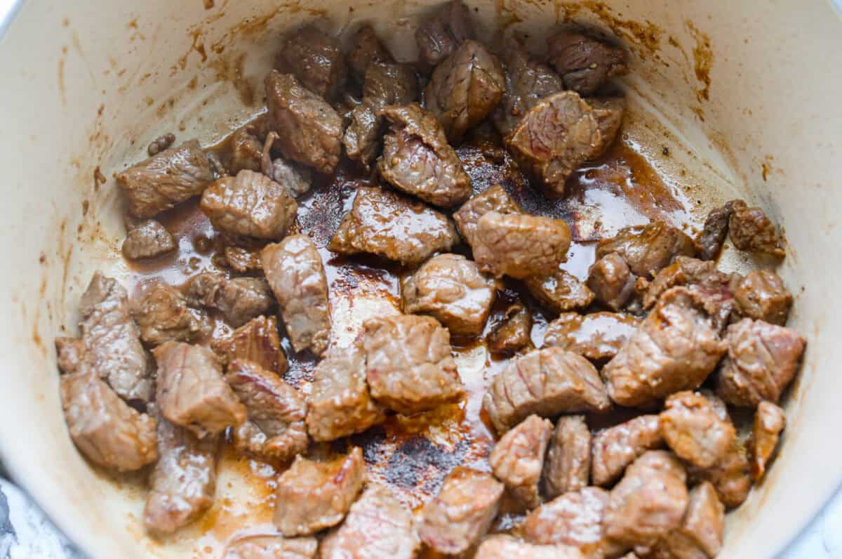 Apple cider beef stew tastes like fall by the spoonful! Tender beef, buttery potatoes, and hearty veggies simmer in a rich broth with apple cider, thyme, and sage for the coziest cold-weather dinner. Beef browning in the bottom of a dutch oven.