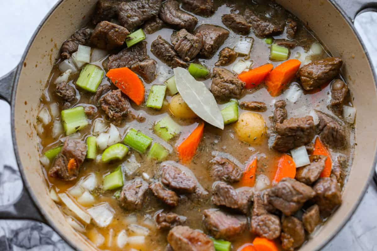 Apple cider beef stew tastes like fall by the spoonful! Tender beef, buttery potatoes, and hearty veggies simmer in a rich broth with apple cider, thyme, and sage for the coziest cold-weather dinner. Stew ingredients added to a large pot to simmer and cook.
