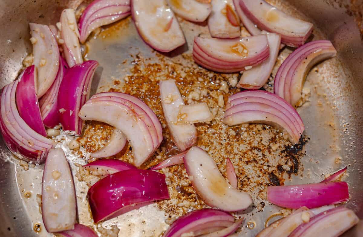 If you love a good Sunday roast, this apple cider pork roast needs to be on your fall menu. Tender pork cooks with apple cider, herbs, and sweet-tart apples until it’s fall-apart tender and perfect over creamy mashed potatoes. Garlic and onions sautéing in olive oil.