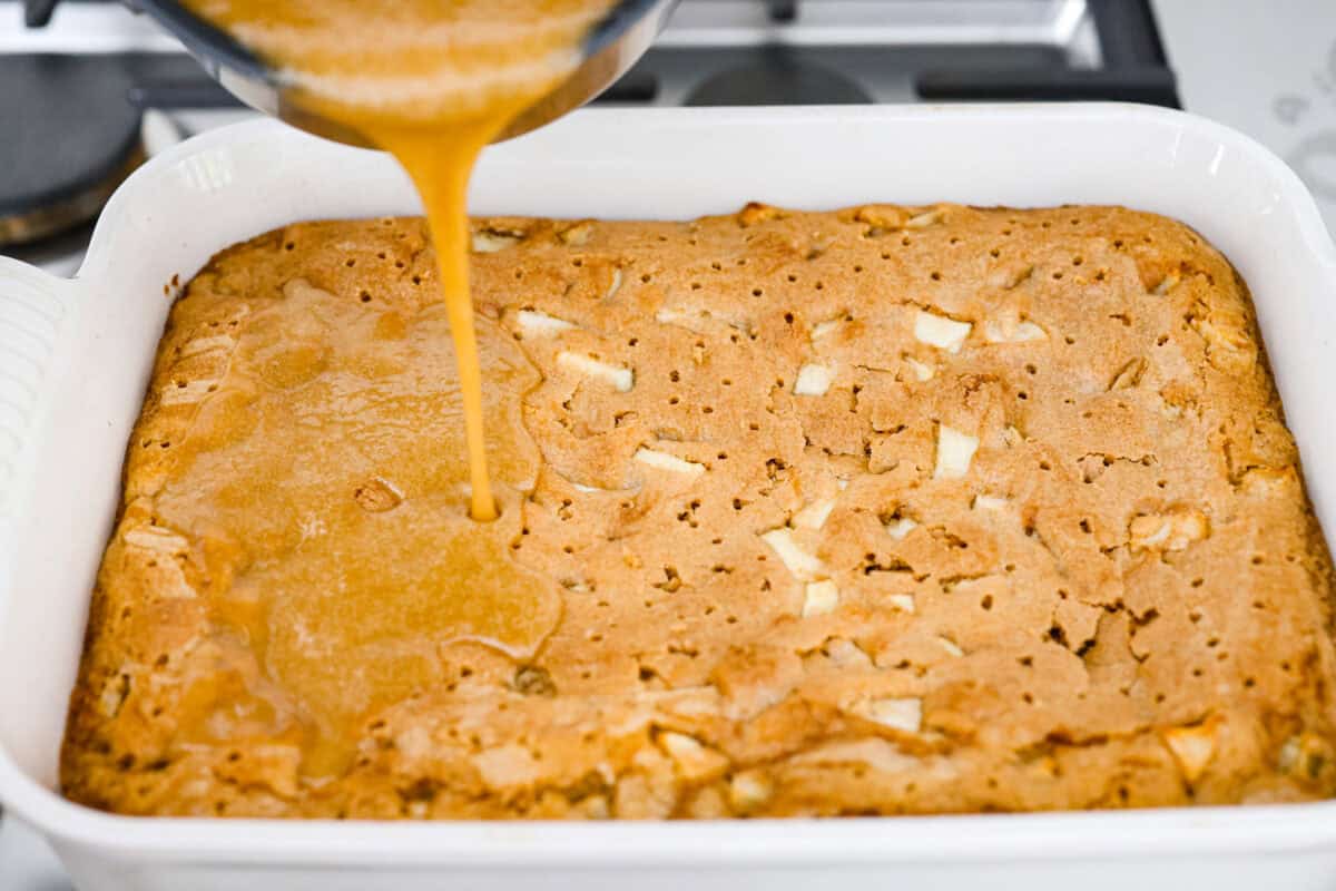 If you love cozy apple desserts, this apple dapple cake is going to be your new fall favorite. It’s packed with fresh apples and warm cinnamon, topped with a buttery caramel glaze that sinks right into the cake. Caramel glaze being poured over the baked apple dapple cake that has been poked with holes.