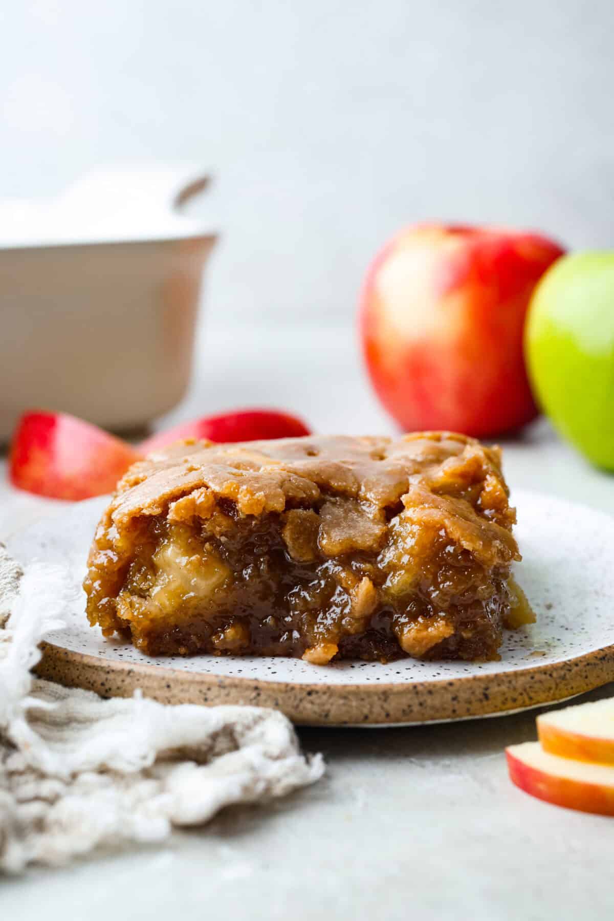 If you love cozy apple desserts, this apple dapple cake is going to be your new fall favorite. It’s packed with fresh apples and warm cinnamon, topped with a buttery caramel glaze that sinks right into the cake. Slice of apple dapple cake with apples behind it.