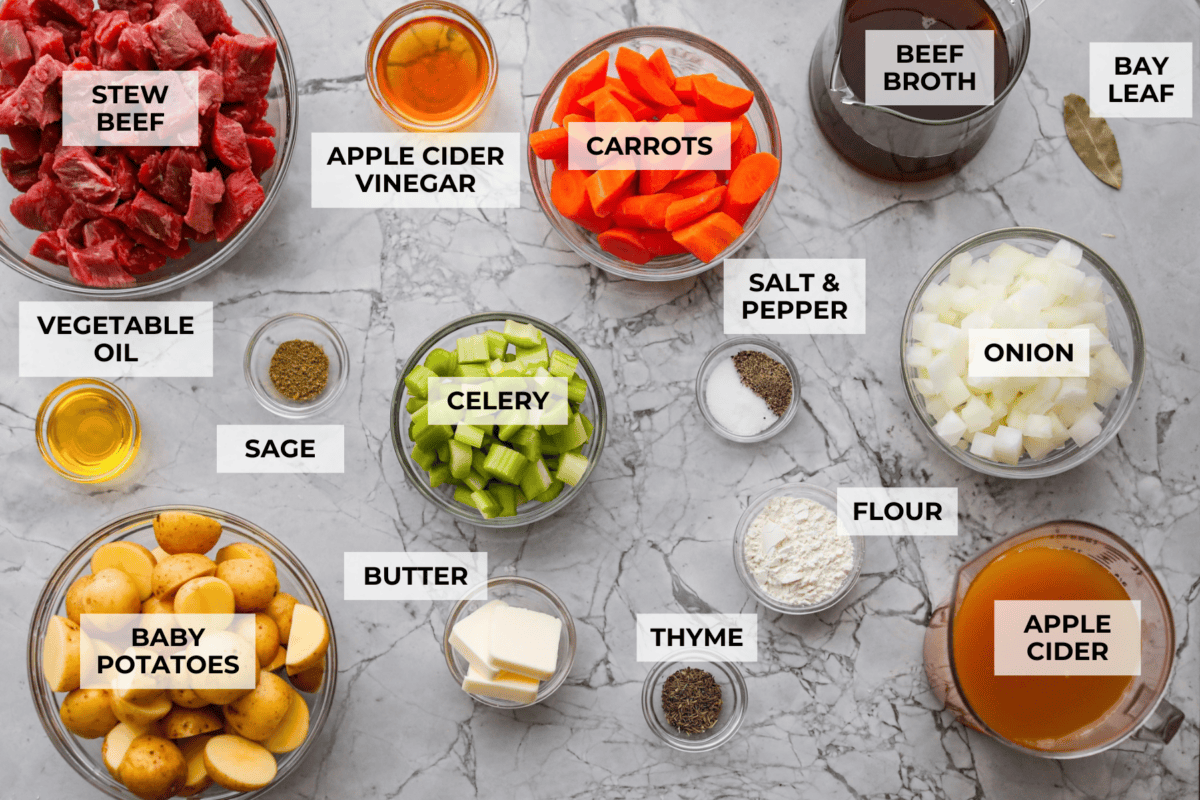 Apple cider beef stew tastes like fall by the spoonful! Tender beef, buttery potatoes, and hearty veggies simmer in a rich broth with apple cider, thyme, and sage for the coziest cold-weather dinner. Overhead shot of labeled apple cider beef stew ingredients.