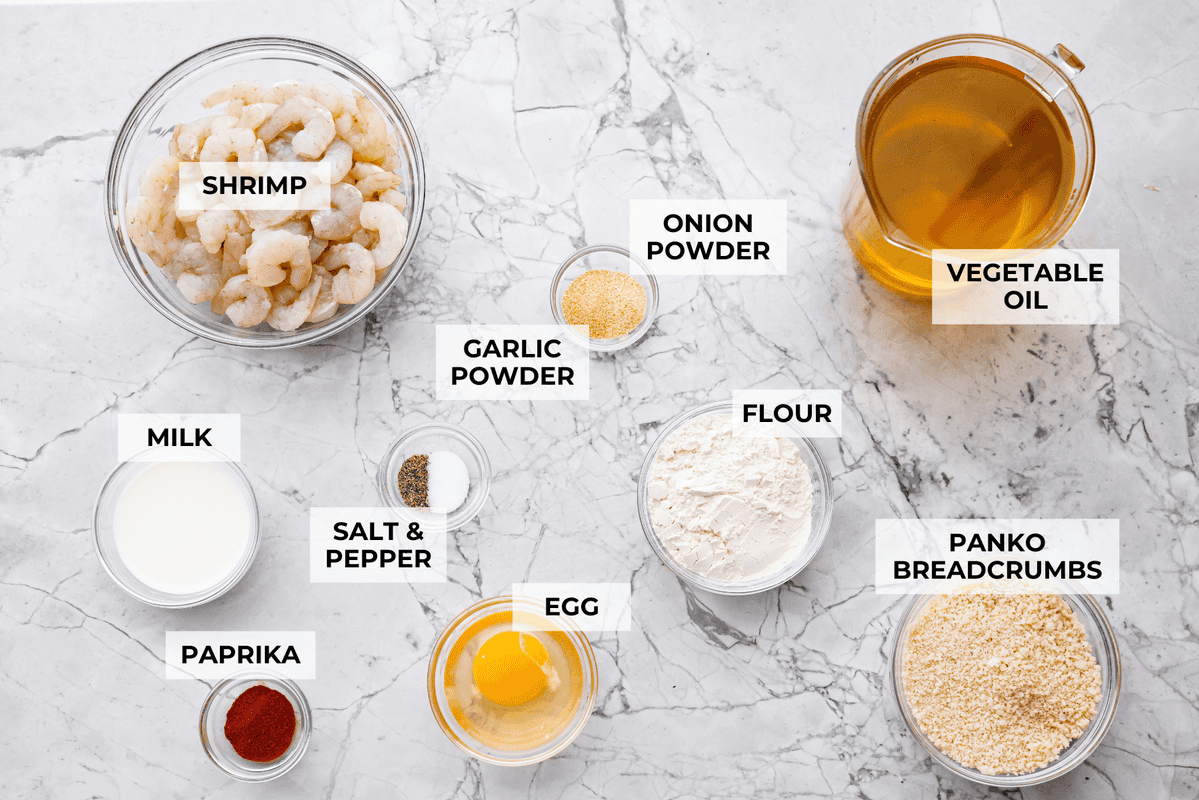 These crispy popcorn shrimp are little bites of golden, crunchy goodness! Juicy shrimp get coated in seasoned panko and fried until perfectly crisp. Serve them hot with a squeeze of lemon and cocktail sauce for dipping! Overhead shot of labeled crispy popcorn shrimp ingredients.